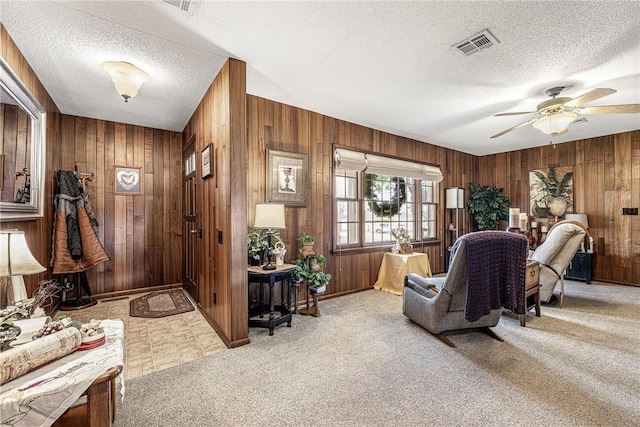 carpeted living room featuring wooden walls, a textured ceiling, and ceiling fan