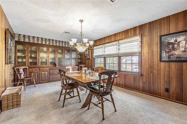 carpeted dining space with wooden walls, a textured ceiling, and an inviting chandelier