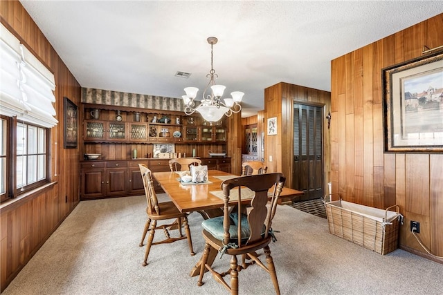 dining space with light carpet, a notable chandelier, built in shelves, and wood walls