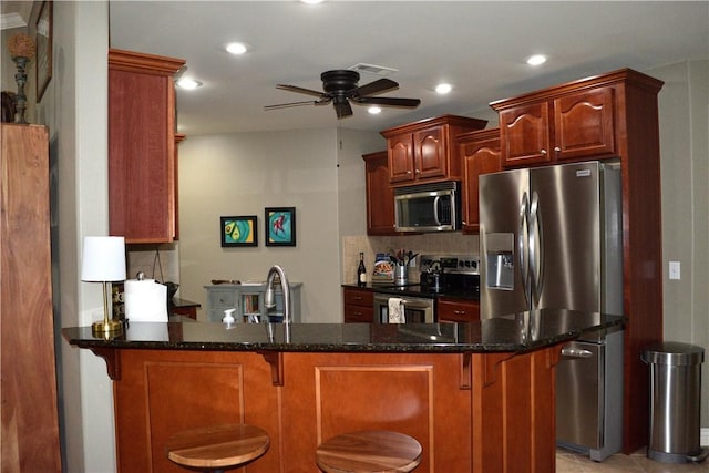 kitchen with backsplash, dark stone counters, ceiling fan, kitchen peninsula, and stainless steel appliances