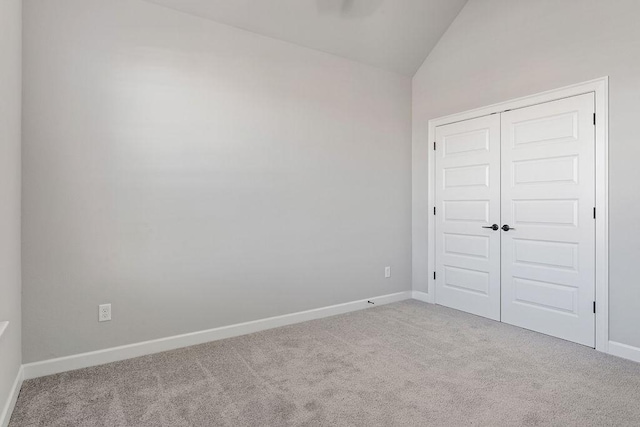 unfurnished bedroom featuring vaulted ceiling, a closet, and light colored carpet