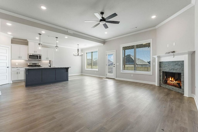 unfurnished living room with a fireplace, wood-type flooring, ornamental molding, ceiling fan with notable chandelier, and sink