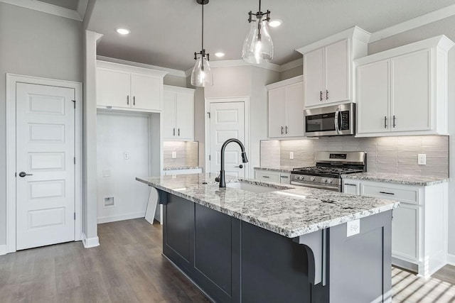 kitchen with sink, white cabinetry, hanging light fixtures, appliances with stainless steel finishes, and an island with sink