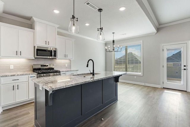 kitchen with an island with sink, appliances with stainless steel finishes, hanging light fixtures, white cabinets, and sink