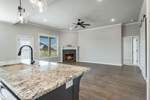 kitchen with ceiling fan, a kitchen island with sink, a fireplace, hanging light fixtures, and sink