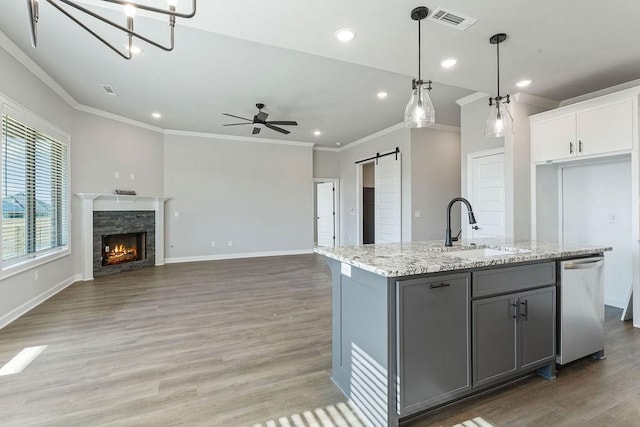 kitchen featuring stainless steel dishwasher, white cabinets, a kitchen island with sink, and a barn door