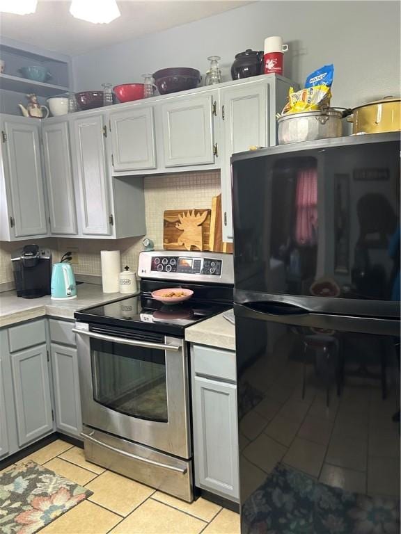 kitchen featuring gray cabinetry, backsplash, black fridge, light tile patterned flooring, and stainless steel electric range