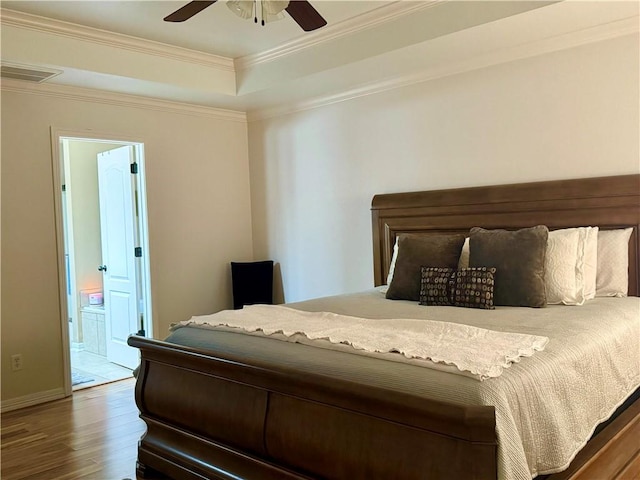 bedroom with ensuite bathroom, ceiling fan, a tray ceiling, hardwood / wood-style flooring, and ornamental molding