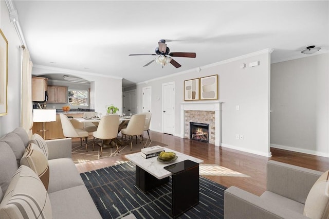 living room featuring ceiling fan, a stone fireplace, crown molding, and wood-type flooring