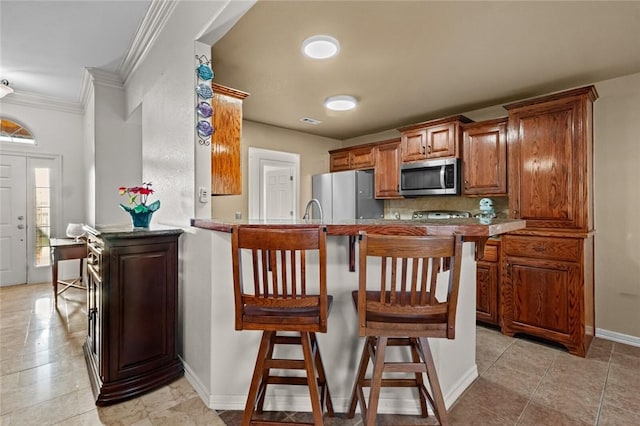 kitchen with kitchen peninsula, a kitchen bar, sink, ornamental molding, and stainless steel appliances