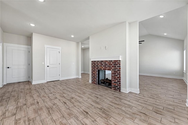 unfurnished living room featuring wood finished floors, baseboards, lofted ceiling, recessed lighting, and a brick fireplace