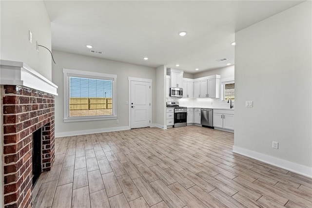 unfurnished living room with a wealth of natural light, visible vents, baseboards, and light wood-style floors