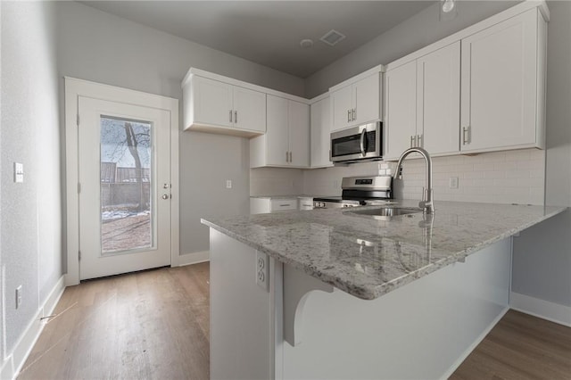 kitchen with sink, white cabinetry, light wood-type flooring, light stone countertops, and stainless steel appliances