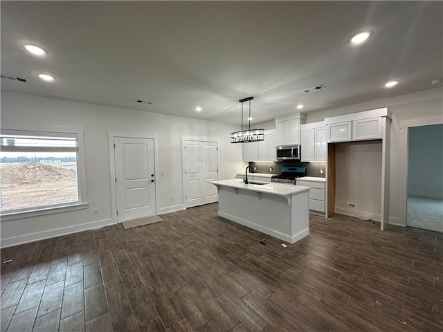 kitchen featuring white cabinetry, a center island with sink, appliances with stainless steel finishes, dark wood-type flooring, and hanging light fixtures