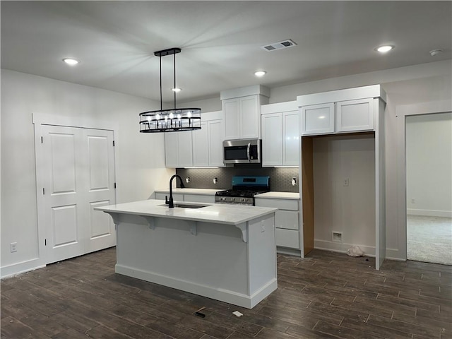 kitchen featuring decorative light fixtures, white cabinetry, stainless steel appliances, sink, and a kitchen island with sink