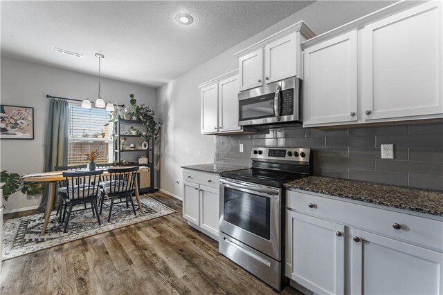 kitchen with stainless steel appliances, backsplash, dark wood-type flooring, dark stone countertops, and white cabinets