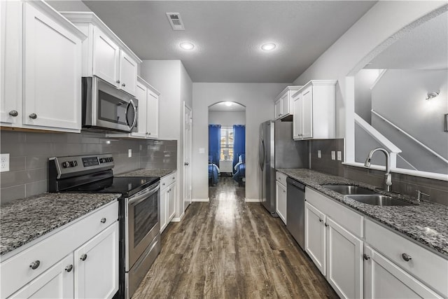 kitchen with arched walkways, white cabinets, dark wood-style floors, stainless steel appliances, and a sink