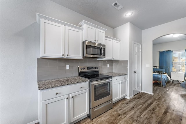 kitchen featuring backsplash, white cabinets, stainless steel appliances, and dark stone countertops