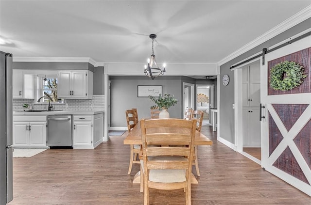 dining area with an inviting chandelier, a barn door, ornamental molding, light hardwood / wood-style flooring, and sink