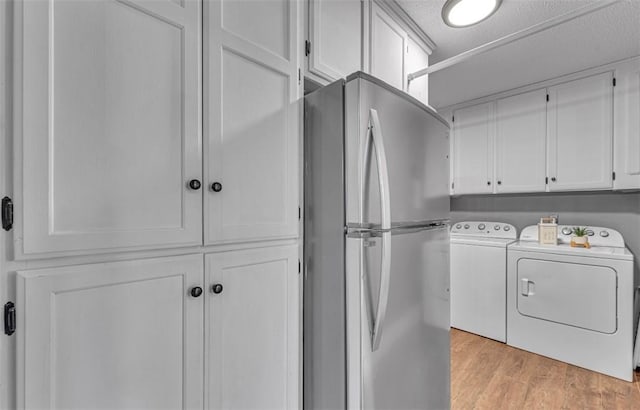 laundry area featuring light hardwood / wood-style floors, a textured ceiling, washing machine and clothes dryer, and cabinets