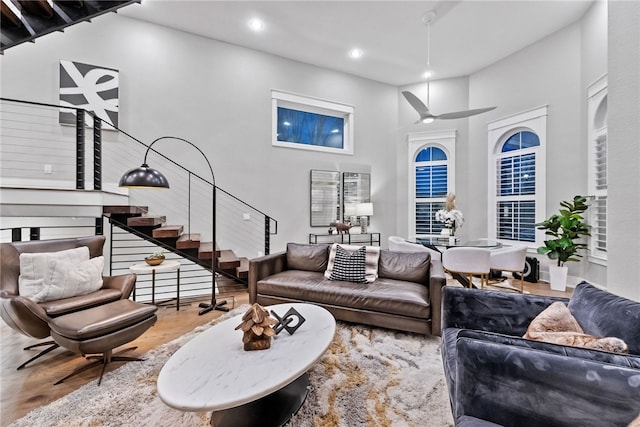 living room with ceiling fan, a towering ceiling, and hardwood / wood-style flooring