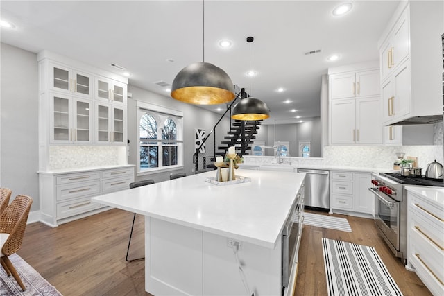 kitchen featuring a breakfast bar area, stainless steel appliances, decorative light fixtures, white cabinets, and a center island