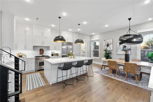 kitchen with decorative light fixtures, white cabinetry, light wood-type flooring, and high quality appliances