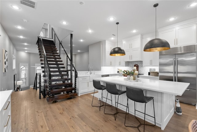 kitchen featuring white cabinetry, light hardwood / wood-style floors, stainless steel built in fridge, tasteful backsplash, and decorative light fixtures