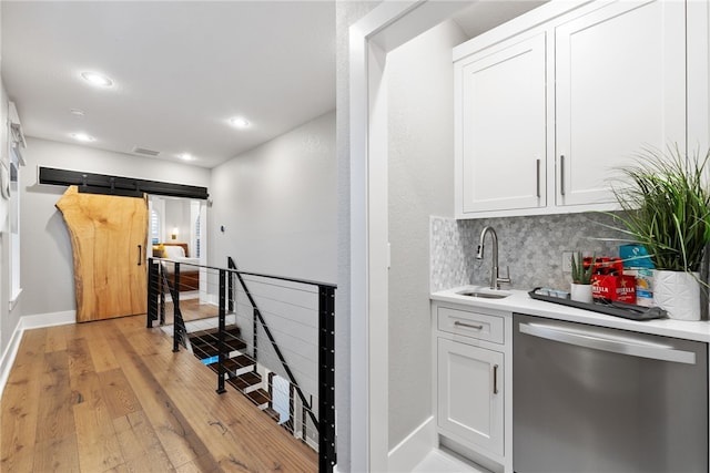 bar featuring white cabinetry, tasteful backsplash, light hardwood / wood-style floors, sink, and stainless steel dishwasher