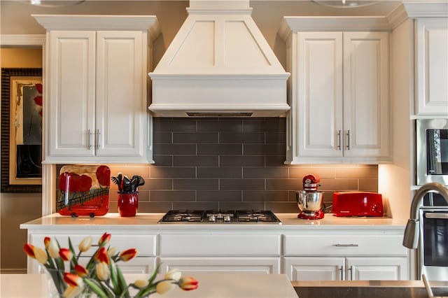 kitchen with tasteful backsplash, stainless steel gas cooktop, white cabinetry, and custom range hood