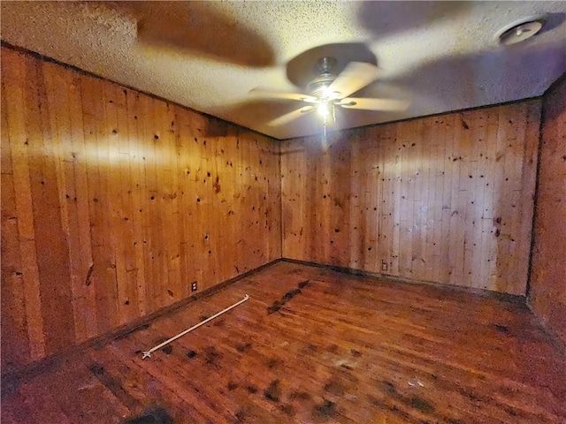 unfurnished room with wood walls, wood finished floors, a textured ceiling, and ceiling fan