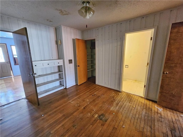 unfurnished bedroom featuring hardwood / wood-style flooring, wood walls, and a textured ceiling