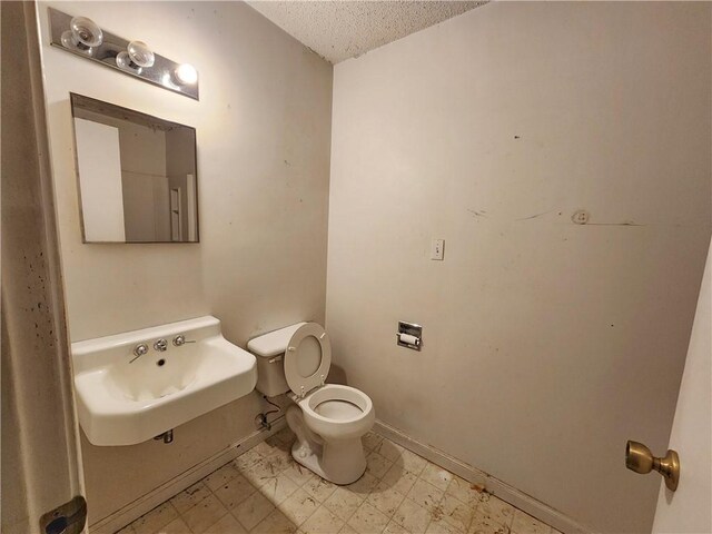 bathroom featuring tile patterned floors, toilet, a sink, baseboards, and a textured ceiling