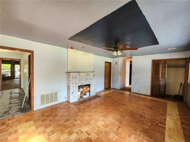 unfurnished living room with ceiling fan, a large fireplace, a raised ceiling, baseboards, and visible vents