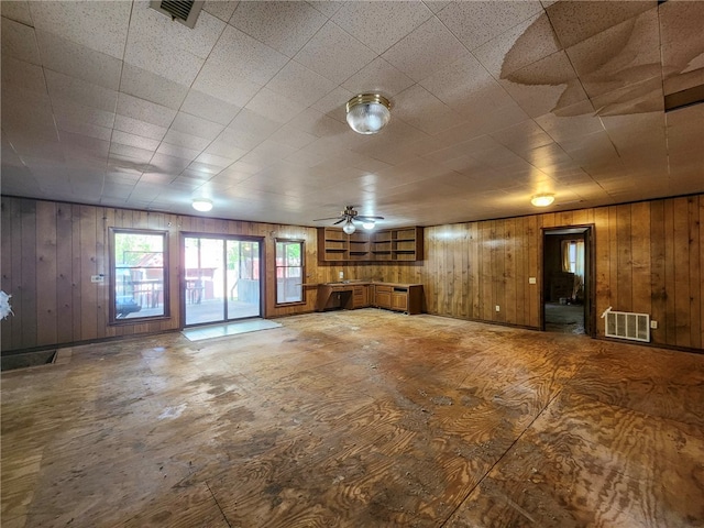 unfurnished living room with wooden walls, a ceiling fan, and visible vents