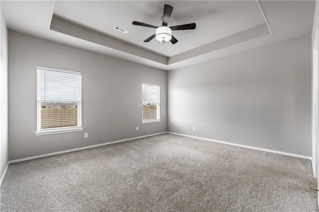 carpeted spare room with ceiling fan and a tray ceiling