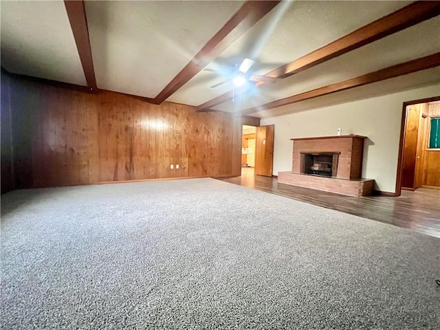 unfurnished living room featuring ceiling fan, beam ceiling, and wood walls