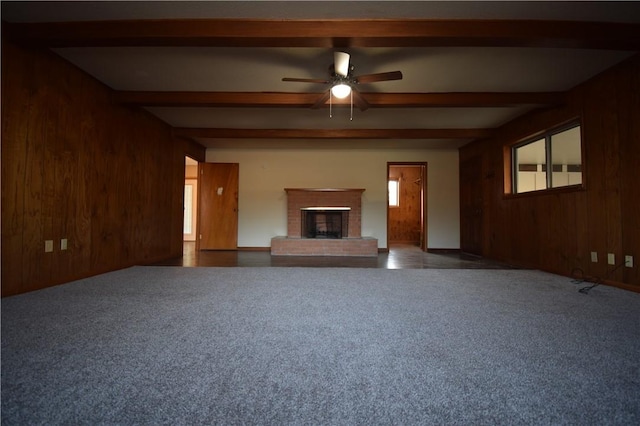 unfurnished living room featuring beamed ceiling, a fireplace, wooden walls, and ceiling fan