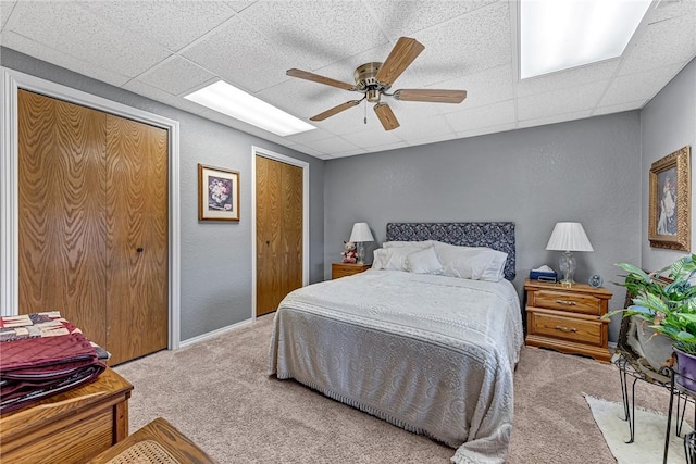 carpeted bedroom featuring ceiling fan, a paneled ceiling, and multiple closets