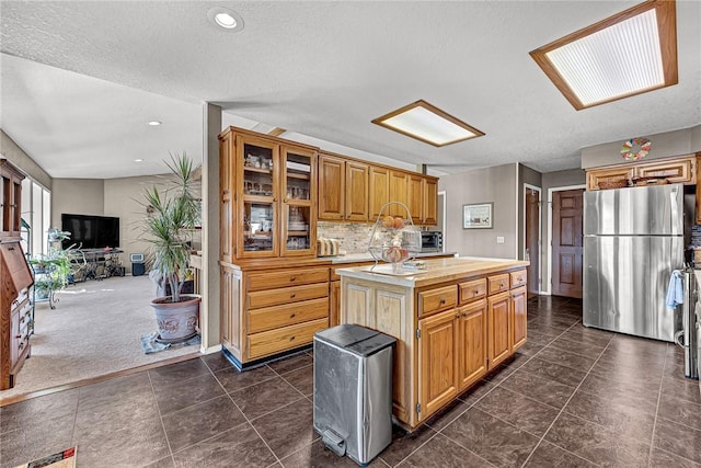 kitchen with a textured ceiling, dark carpet, stainless steel refrigerator, decorative backsplash, and a kitchen island