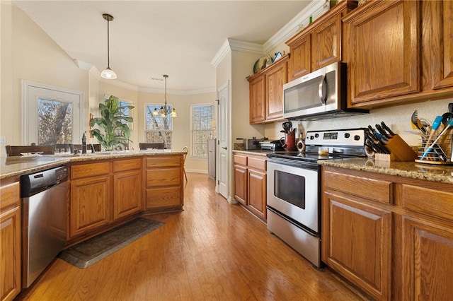 kitchen with pendant lighting, appliances with stainless steel finishes, sink, light stone countertops, and light hardwood / wood-style floors