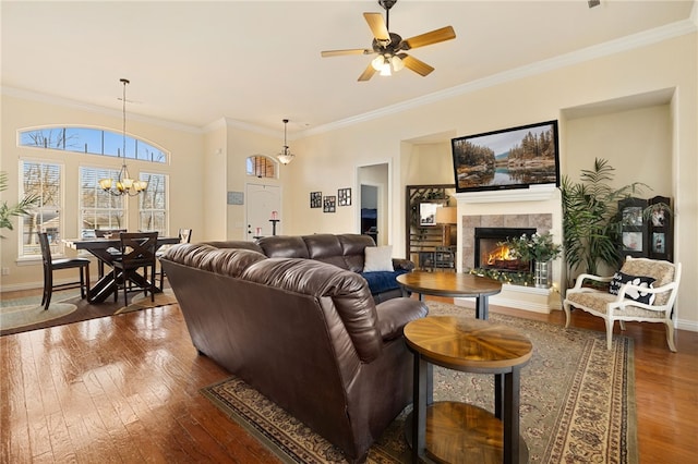 living room with hardwood / wood-style flooring, ceiling fan with notable chandelier, crown molding, and a fireplace