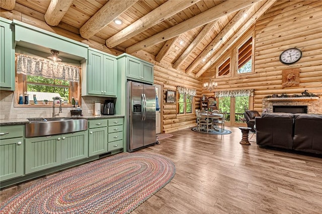 kitchen featuring stainless steel refrigerator with ice dispenser, light hardwood / wood-style flooring, sink, green cabinetry, and rustic walls