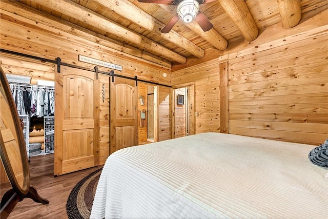 bedroom with hardwood / wood-style flooring, wooden ceiling, a barn door, and wooden walls