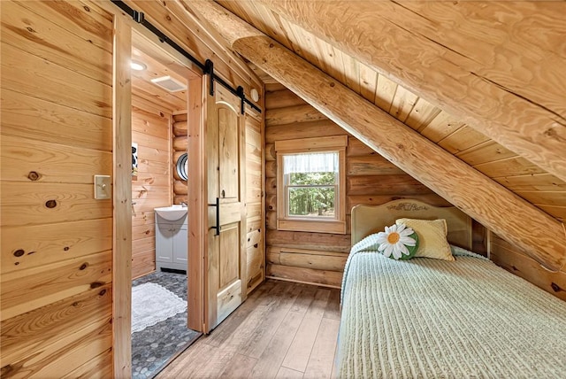 unfurnished bedroom with log walls, a barn door, wooden ceiling, hardwood / wood-style floors, and connected bathroom