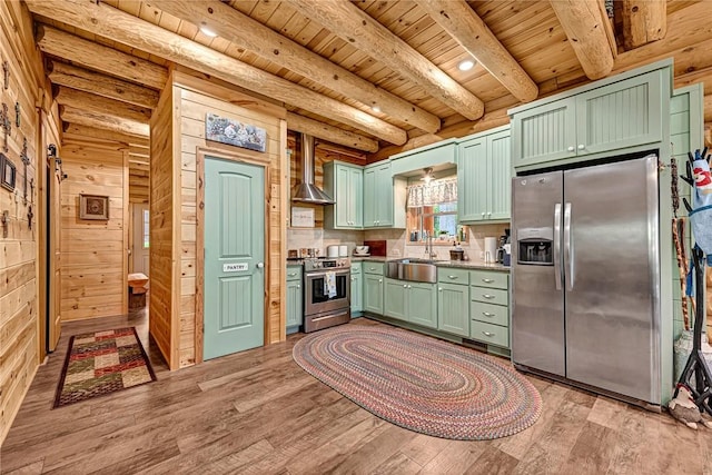 kitchen with wooden walls, green cabinets, wall chimney range hood, and appliances with stainless steel finishes