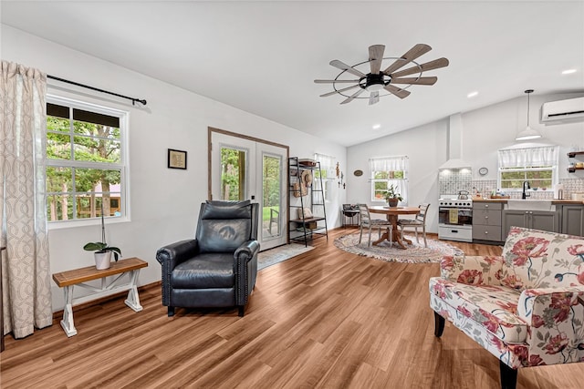 living area featuring light hardwood / wood-style flooring, french doors, sink, a wall mounted AC, and lofted ceiling