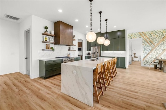 kitchen featuring light stone countertops, hanging light fixtures, sink, light wood-type flooring, and a center island with sink