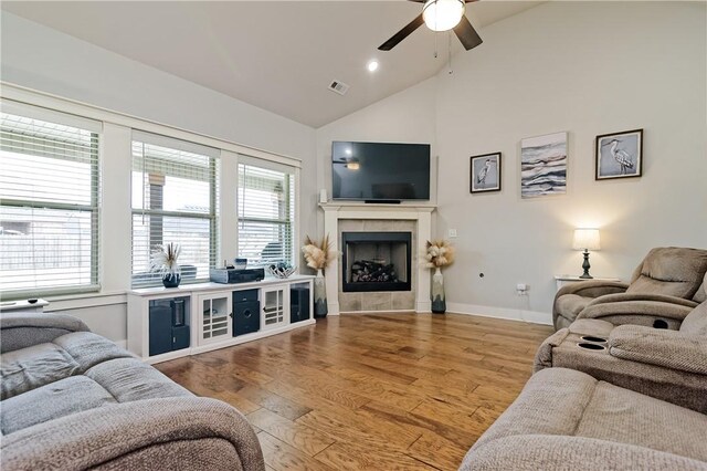 living room featuring hardwood / wood-style floors, a tiled fireplace, high vaulted ceiling, and ceiling fan