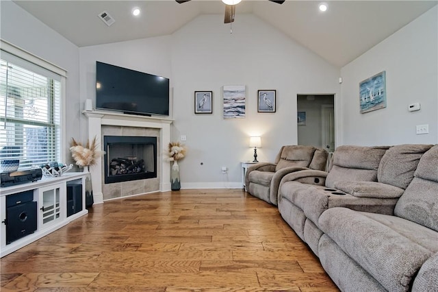 living room with a tiled fireplace, vaulted ceiling, ceiling fan, and light hardwood / wood-style flooring